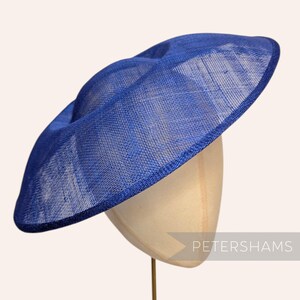 May include: A wide-brimmed royal blue hat with a woven, textured finish and a structured, slightly angled crown. The hat features a solid blue edge binding and is displayed on a neutral-toned mannequin head. The text PETERSHAMS is visible.