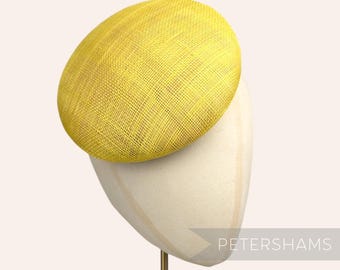 May include: A bright yellow, round hat made of woven straw. The hat is sitting on a white hat form.