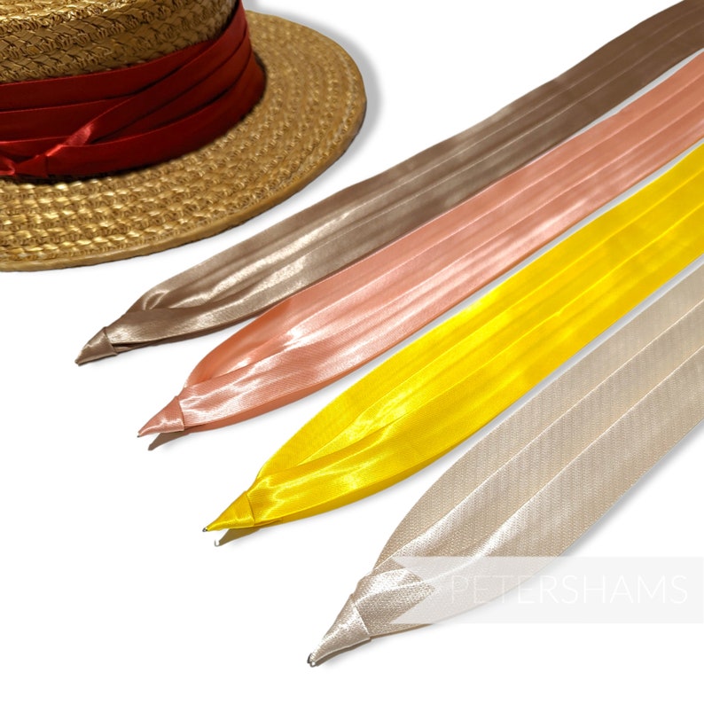 May include: Four different colors of satin ribbon, including beige, peach, yellow, and ivory. The ribbons are arranged in a fan shape, with the beige ribbon at the top and the ivory ribbon at the bottom. The ribbons are all about 1 inch wide and are made of a soft, silky fabric.