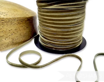 May include: A spool of olive green velvet ribbon. The ribbon is 1/4 inch wide and is wound around a black spool. The ribbon is lying on a wooden surface.