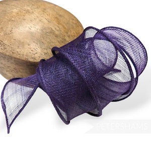 May include: Purple mesh ribbon with a fine, woven texture. The ribbon is folded and twisted into a decorative shape.