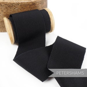 Könnte beinhalten: Schwarzes Grosgrainband auf einer Holzspule. Das Band ist 2,5 cm breit und hat eine glatte, satinartige Oberfläche. Das Band ist perfekt zum Basteln, Nähen und Dekorieren.