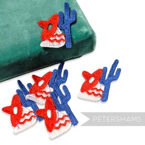 Könnte beinhalten: Gestickte Aufnäher mit einem rot-weiß-blauen Sombrero und einem blauen Kaktus. Die Aufnäher sind auf einer grünen Oberfläche und einem weißen Hintergrund angeordnet. Das Wort "PETERSHAMS" ist unten rechts zu sehen.