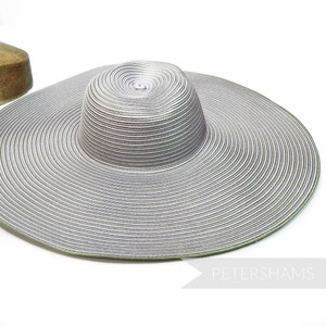 May include: A wide-brimmed sun hat in silver and green. The hat features a circular crown and a broad, gently sloping brim. The hat's surface has a ribbed texture. The text "PETERSHAMS" is visible in the lower right corner.
