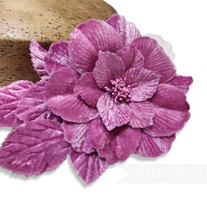 Può includere: Un fiore di velluto magenta con più petali e foglie. Il fiore ha un centro dettagliato ed è posto su uno sfondo bianco. Il fiore è un oggetto decorativo.