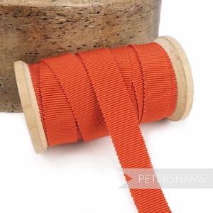 May include: A spool of orange grosgrain ribbon. The ribbon is wound around a wooden spool and is ready to be used for crafting or decorating.