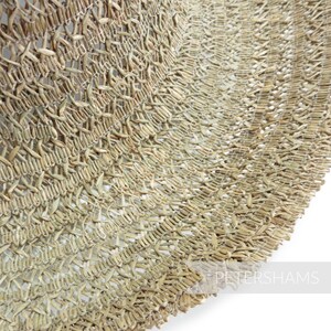May include: Close-up of a woven straw hat, showing the intricate details of the natural material. The hat is light brown in color and has a slightly curved brim.