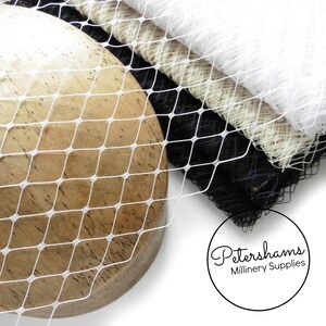 May include: White, black, and beige netting fabric. The netting is a diamond pattern. The fabric is folded and draped over a wooden surface. The text "Petershams Millinery Supplies" is visible in the lower right corner of the image.