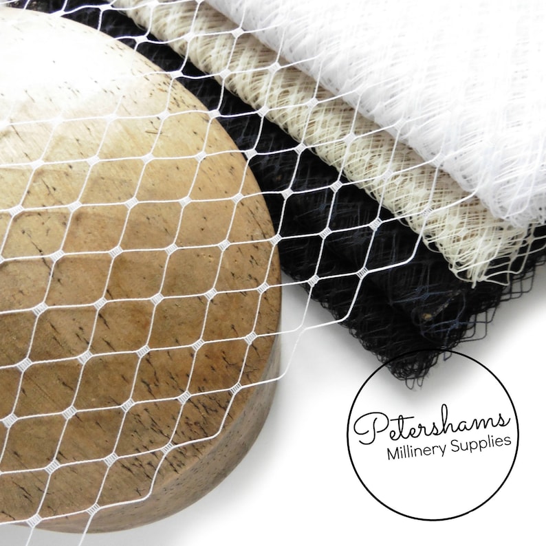 May include: White, black, and beige netting fabric. The netting is a diamond pattern. The fabric is folded and draped over a wooden surface. The text "Petershams Millinery Supplies" is visible in the lower right corner of the image.