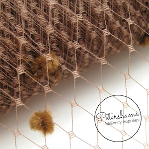 May include: Close-up of brown netting fabric with small brown pom-poms. The fabric is rolled up and the netting is visible. The text "Petershams Millinery Supplies" is visible in a circle.