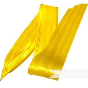 Pode incluir: Uma fita de cetim amarelo brilhante, dobrada e disposta de forma decorativa. A fita &eacute; lisa e brilhante, com um leve brilho. &Eacute; uma fita vers&aacute;til que pode ser usada para uma variedade de prop&oacute;sitos, como embrulhar presentes, decorar artesanato ou adicionar um toque de eleg&acirc;ncia a qualquer projeto.