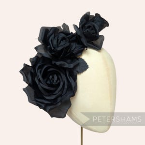 Könnte beinhalten: Ein schwarzes Kopfstück mit Stoffrosen. Mehrere Rosen unterschiedlicher Größe sind zu einer auffälligen Anordnung zusammengefasst. Das Kopfstück wird auf einem Mannequinkopf präsentiert. Das Wort "PETERSHAMS" ist sichtbar.
