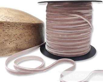 May include: A spool of dusty rose velvet ribbon sits next to a wooden form. The ribbon is unwound, revealing its soft texture. The spool is on a black base. The ribbon is approximately 0.25 inches wide.