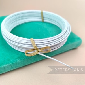 May include: A spool of white Petershams ribbon tied with a brown ribbon. The ribbon is on a teal surface.