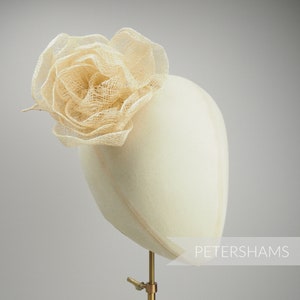 May include: A delicate, off-white, fabric flower hair accessory. The flower is made of a woven, mesh-like material and is displayed on a white mannequin head.