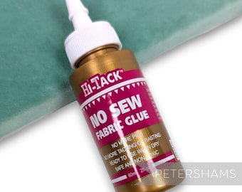 May include: A gold bottle of Hi-Tack No Sew Fabric Glue. The bottle has a pink label with white text that reads "No More Pins, No More Tacking of Basting, Ready to Use When Dry, Safe and Non Toxic". The bottle is 60ml or 2 fl oz.