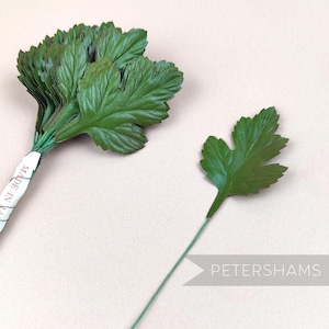 Op de afbeelding: Een bos groene kunstmatige bladeren met een draadsteel, en een enkel groen blad met een draadsteel. De bladeren zijn gemaakt van een getextureerd materiaal dat eruitziet als leer. De tekst "MADE IN" is zichtbaar op het etiket van het bos bladeren.