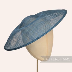 May include: A blue hat with a wide brim, displayed on a mannequin head. The hat has a woven texture and a slightly curved shape. The brim is edged with a darker blue trim. The hat is suitable for formal events.
