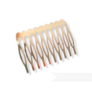 May include: A gold-coloured hair comb with a scalloped top edge and ten evenly spaced, elongated oval openings. The comb's teeth are thin and pointed, designed to secure hair. The comb is made of a shiny, metallic material.