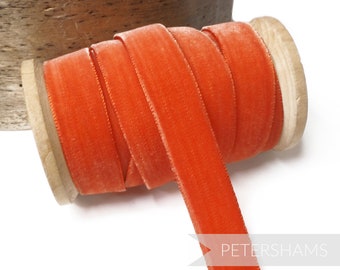 Könnte beinhalten: Eine Spule mit leuchtend orangefarbenem Samtband. Das Band ist um eine Holzspule gewickelt und bereit für Bastelarbeiten oder Dekorationen.