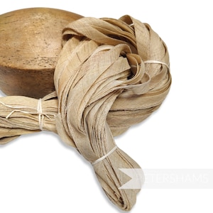 May include: A large bundle of natural beige linen ribbon, tied with a white string. The ribbon is arranged in a loose coil, with some strands hanging loose.