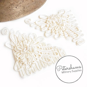 May include: Two white Chinese knot embellishments with pearl accents. The knots are in the shape of a flower and have a traditional design.