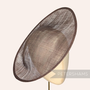 Peut inclure: Chapeau marron de forme ovale avec un large bord. Le chapeau est fait d'un matériau tissé, avec une bordure marron plus foncée sur le bord. Le chapeau est présenté sur une tête de mannequin.