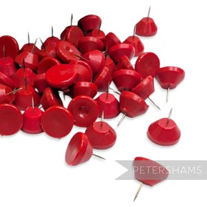 May include: A collection of bright red push pins with silver metal tips. The push pins are scattered on a white background. The push pins have a rounded, conical shape. The text "PETERSHAMS" is in the lower right corner.