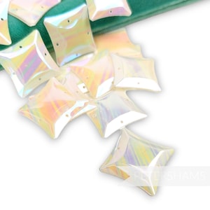May include: A group of iridescent white plastic star-shaped sequins with four points. The sequins have a hole in the center for sewing.