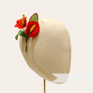 May include: A white mannequin head with a red and yellow flower attached to the side. The flower is a silk flower and is a type of anthurium.