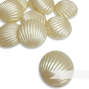 May include: A collection of cream-colored, shell-shaped buttons with a pearlescent finish. The buttons have a ridged texture radiating from the center. The buttons are scattered on a white background.