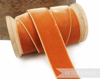 Könnte beinhalten: Eine Spule mit orangefarbenem Samtband. Das Band ist um eine Holzspule gewickelt. Das Band ist glatt und hat einen leichten Glanz.