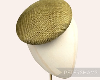 May include: A gold-colored, round, woven hat with a textured surface. The hat is displayed on a white hat form.