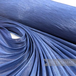 May include: A close-up shot of a roll of blue fabric with a textured, woven appearance. The fabric is draped and folded, creating a sense of depth and texture. The Petershams logo is visible in the bottom right corner.