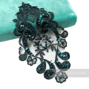 May include: An ornate, dark teal lace applique with teal sequins. The lace features floral and scroll designs. The applique is set against a teal velvet background. The word "PETERSHAMS" is visible in the lower right corner.