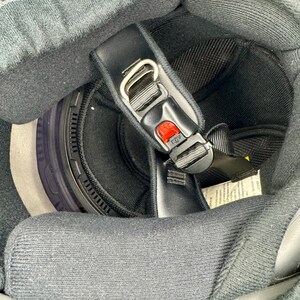 Peut inclure: Vue int&eacute;rieure d'un casque de moto noir. Le casque est dot&eacute; d'une jugulaire noire avec un bouton de d&eacute;verrouillage rouge, d'une doublure int&eacute;rieure noire et d'un tour de cou noir. Le rembourrage int&eacute;rieur du casque est gris.