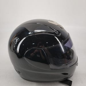 Peut inclure: Casque de moto noir brillant avec une visi&egrave;re teint&eacute;e. Le casque a un design &eacute;pur&eacute; et une jugulaire. Un embl&egrave;me argent&eacute; est visible sur le dessus du casque.
