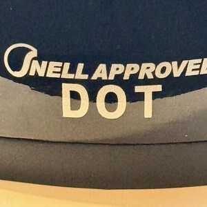 Peut inclure: Gros plan sur une surface bleu fonc&eacute; avec le texte blanc "Snell Approved DOT". Le texte est en police sans-serif. L'image est bien &eacute;clair&eacute;e et le texte est clair et facile &agrave; lire.