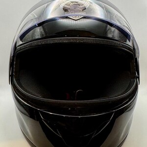 Peut inclure: Casque de moto noir brillant avec une visi&egrave;re transparente. Le casque pr&eacute;sente un logo Harley-Davidson sur le dessus. La visi&egrave;re est l&eacute;g&egrave;rement teint&eacute;e et se courbe &agrave; l'avant. L'int&eacute;rieur est noir.