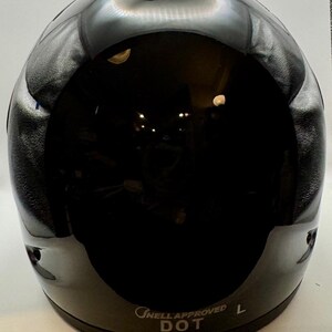 Peut inclure: Casque de moto noir brillant avec une surface lisse et r&eacute;fl&eacute;chissante. Le casque a une forme arrondie avec un petit &eacute;vent en haut. Le texte "ONELL APPROVED DOT L" est imprim&eacute; sur le bord inf&eacute;rieur.