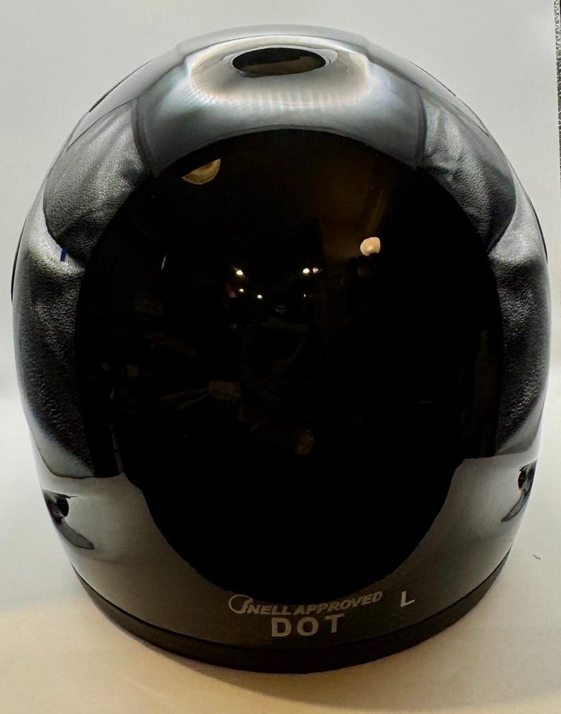 Peut inclure: Casque de moto noir brillant avec une surface lisse et r&eacute;fl&eacute;chissante. Le casque a une forme arrondie avec un petit &eacute;vent en haut. Le texte "ONELL APPROVED DOT L" est imprim&eacute; sur le bord inf&eacute;rieur.