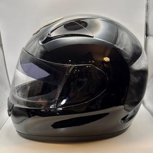Peut inclure: Casque de moto int&eacute;gral noir brillant avec une visi&egrave;re transparente. Le casque a un design &eacute;pur&eacute; avec une visi&egrave;re sombre et un accent argent&eacute; sur le dessus. Con&ccedil;u pour la s&eacute;curit&eacute; et la protection.