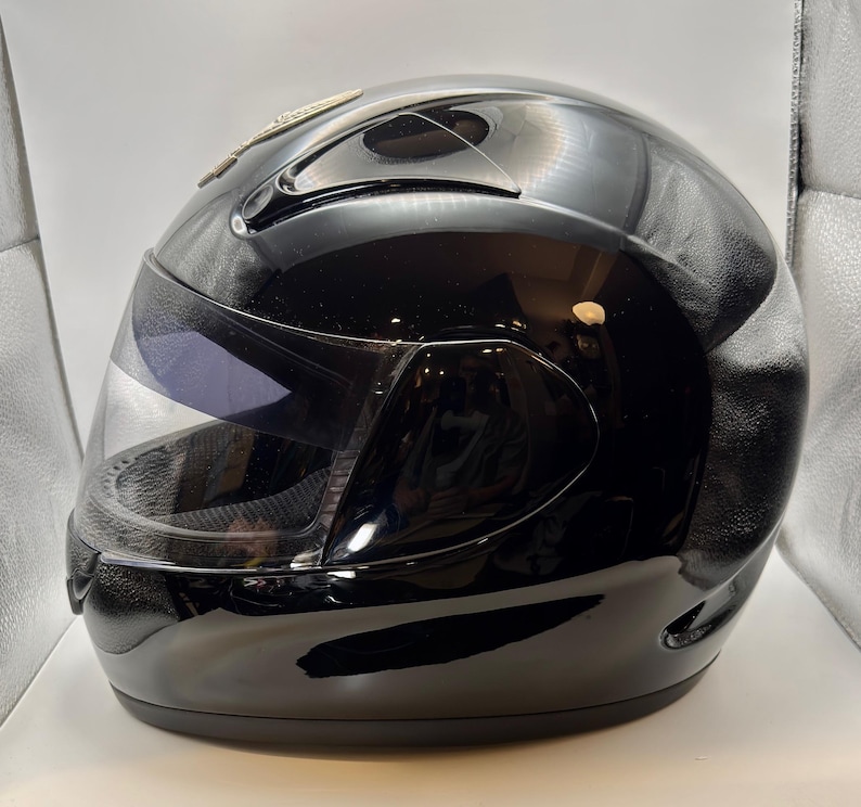 Peut inclure: Casque de moto int&eacute;gral noir brillant avec une visi&egrave;re transparente. Le casque a un design &eacute;pur&eacute; avec une visi&egrave;re sombre et un accent argent&eacute; sur le dessus. Con&ccedil;u pour la s&eacute;curit&eacute; et la protection.