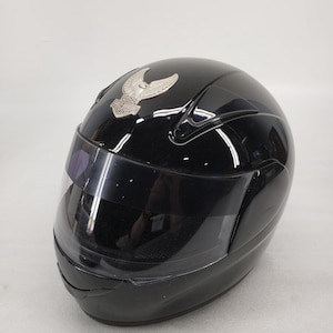 Peut inclure: Casque de moto noir brillant avec visi&egrave;re transparente. Un embl&egrave;me argent&eacute; avec un motif ail&eacute; est fix&eacute; sur le devant. Le casque est con&ccedil;u pour la s&eacute;curit&eacute; et la protection des motocyclistes.