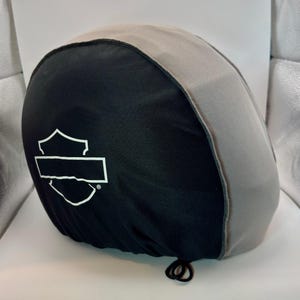 Peut inclure: Housse de casque de moto noire et grise avec un logo blanc. La housse est faite d'un mat&eacute;riau souple et poss&egrave;de une fermeture &agrave; cordon. Le logo est en forme de bouclier avec un espace rectangulaire pour le texte.