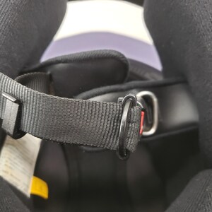 Peut inclure: Gros plan de l'int&eacute;rieur d'un casque de moto noir. L'image met en &eacute;vidence la jugulaire noire avec un anneau en D en m&eacute;tal et un clip en plastique noir. Le rembourrage int&eacute;rieur du casque est visible.