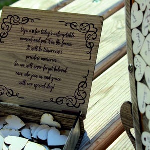 May include: Wooden box with a sign that reads "Sign a heart for today's unforgettable moment and put it in the frame. It will be tomorrow's priceless memories. So, we will never forget beloved ones who join us and grace with our special day!" The box is filled with small wooden hearts.