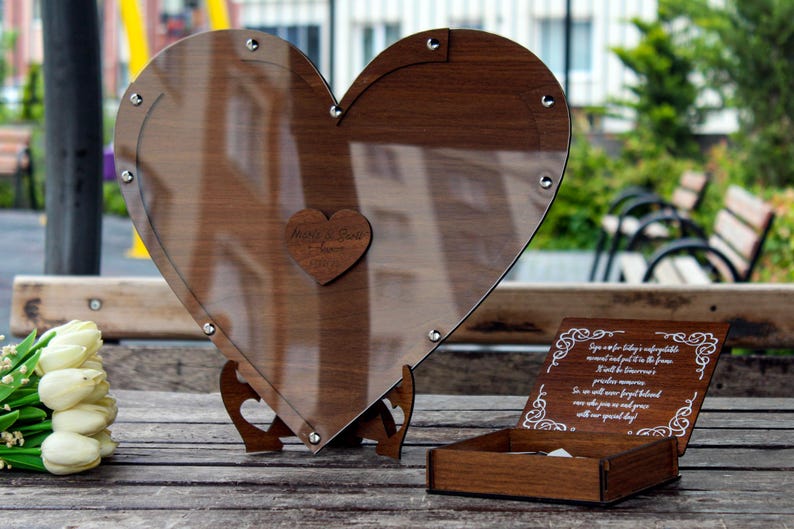 May include: A heart-shaped wooden box with a clear glass lid, a small wooden heart with the words "Always & Forever" engraved on it, and a smaller wooden box with a white inscription on the lid. The boxes are on a wooden surface.