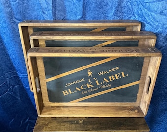 May include: Three wooden trays stacked on top of each other. The top tray has a black background with gold lettering that reads "JOHNNIE WALKER BLACK LABEL Old Scotch Whiskey".
