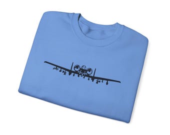 May include: A light blue sweatshirt featuring a black graphic of a military aircraft. The aircraft design is centered on the front of the shirt. The sweatshirt is folded, showing the crew neck and the soft fabric.